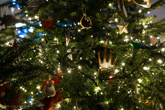 Handcrafted wooden chess ornaments hanging on a Christmas tree branch, showcasing natural Ash and Walnut grain against pine needles. Minimalist, eco-friendly holiday decor in Slow Design style. Photo by Monika Burszczan